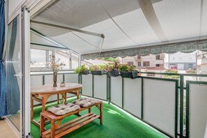A balcony with a wooden table and bench, green artificial turf, potted plants, and a view of buildings in the background. - Spacious apartment Zvone with 3 balconies and parking (Split)