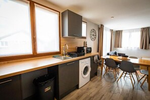Cocina compacta con lavadora, un lavamanos y comedor con mesa y sillas.