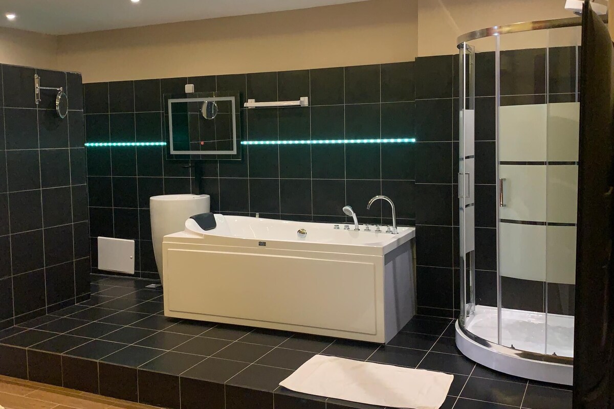Een moderne badkamer met een ruim bad, een douche met glazen wanden en LED-verlichting langs de muur.