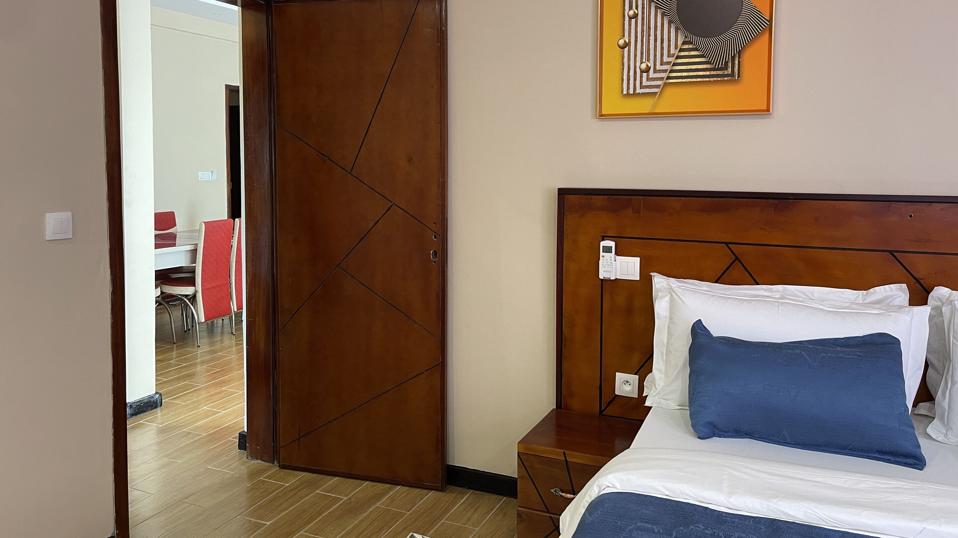 Een hotelkamer met een houten hoofdeinde, een bed met wit en blauw beddegoed, een nachtkastje en een wanddecoratie.
