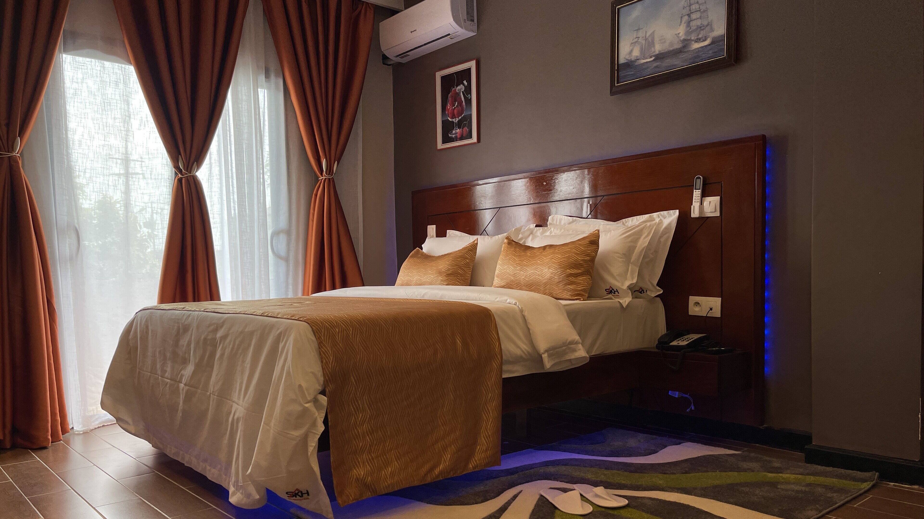 Hotelkamer met een bed, gordijnen, een wandairco, een inlijsting foto en een nachtkastje met een telefoon.