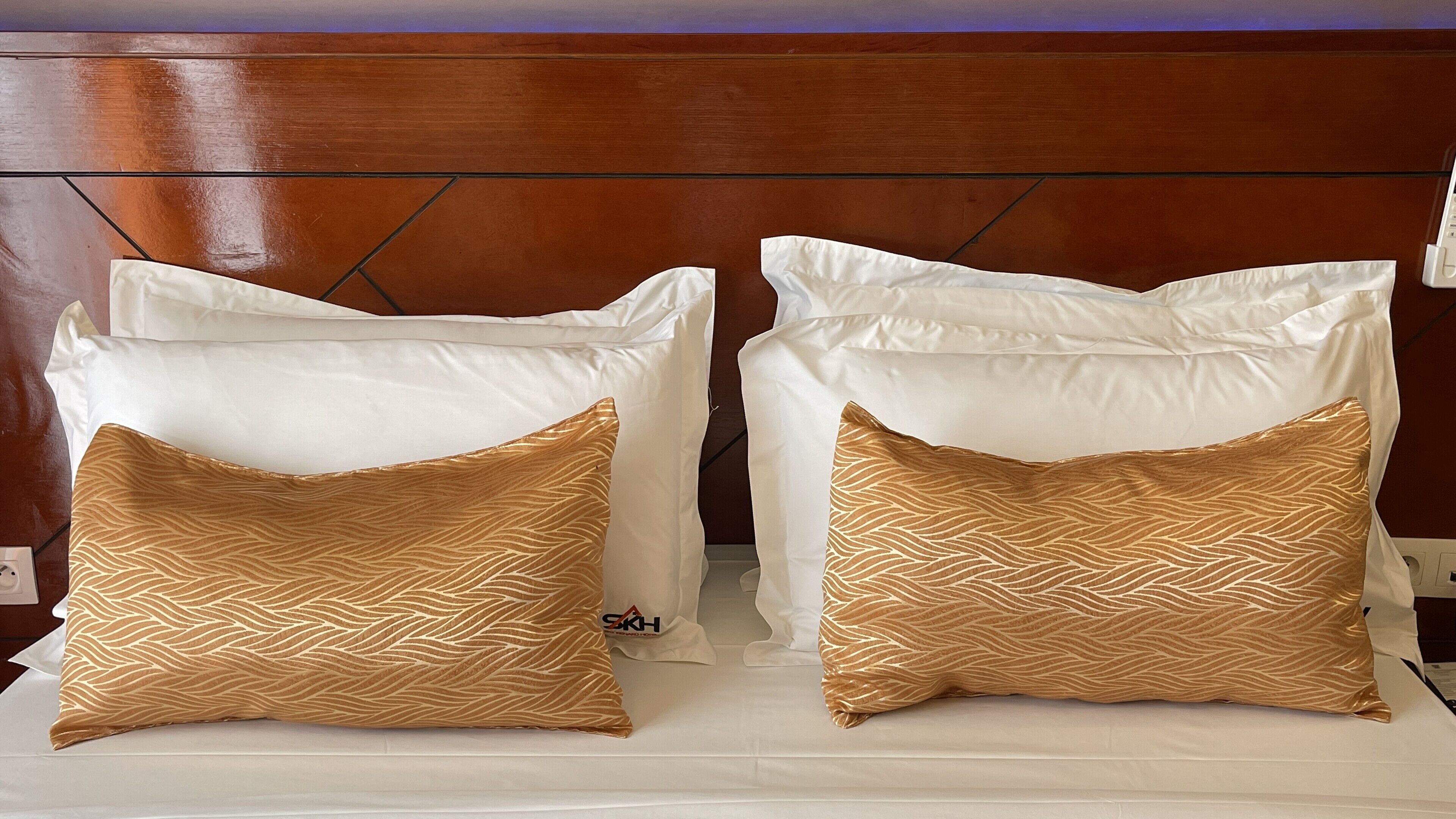 A bed with white pillows and two decorative pillows with a gold pattern.
