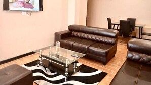 Una sala moderna con un sofá de cuero, una mesa de centro de vidrio y un televisor de pantalla plana montado en la pared.