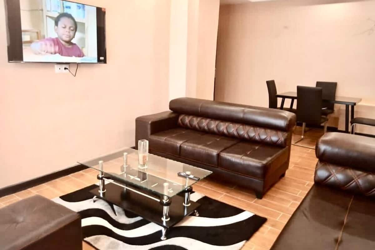 Un salon moderne avec un canapé en cuir, une table basse en verre et un téléviseur à écran plat fixé au mur.