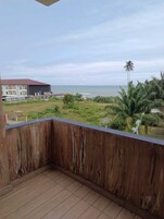 Un balcón con vista al mar, un edificio y algo de vegetación.