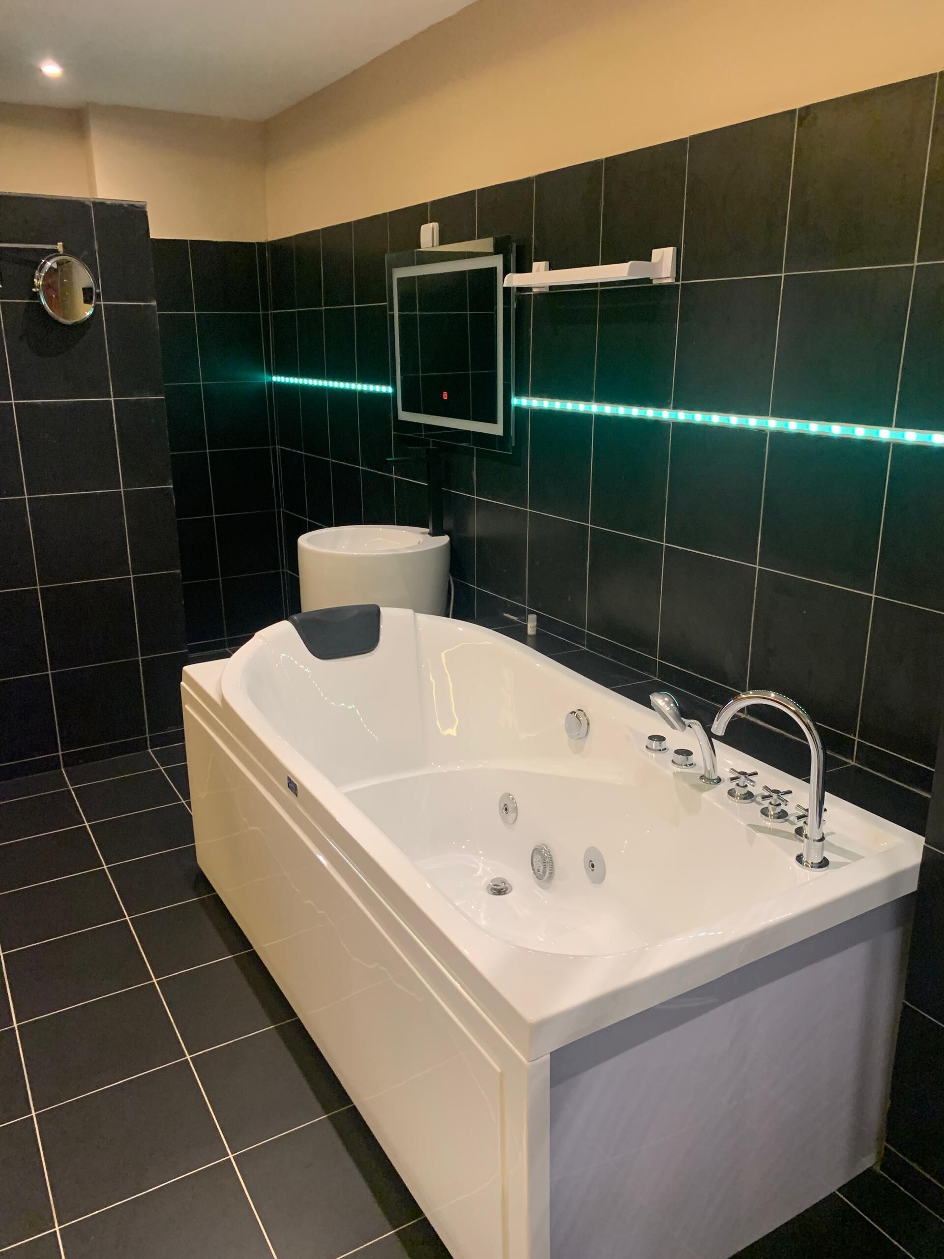 A modern bathroom with a large white bathtub, a toilet, and a sink.