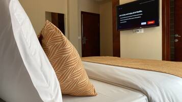 Quarto de hotel com uma cama, televisão presa na parede e uma porta ao fundo.