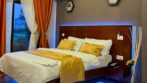 Un dormitorio moderno con una cama grande, un equipo de aire acondicionado, una mesita de noche con un teléfono y un jarrón decorativo.