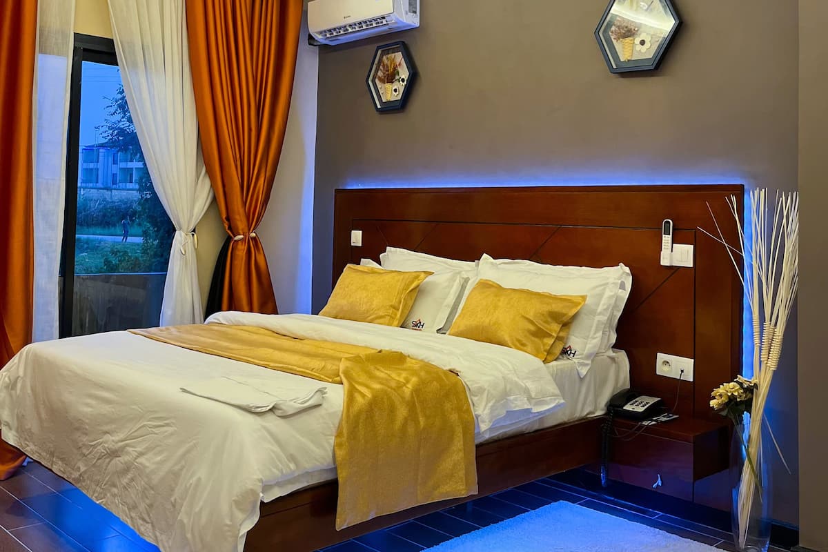 Une chambre moderne avec un grand lit, un appareil de climatisation, une table de chevet avec un téléphone et un vase décoratif.