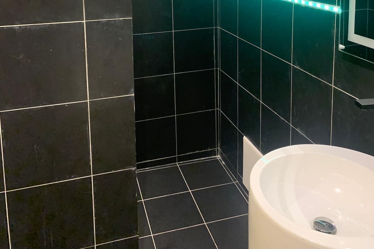Une salle de bain avec des carreaux noirs, un lavabo blanc et un miroir.