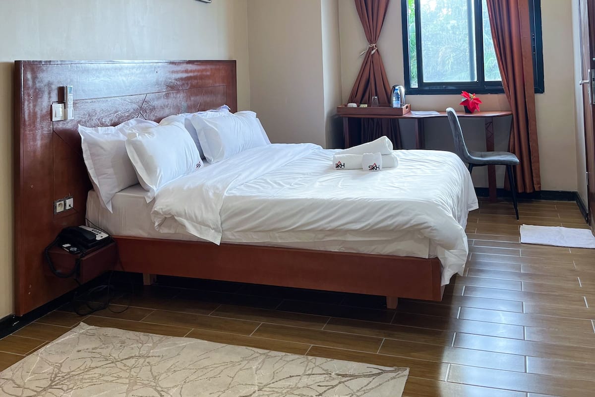 Une chambre d’hôtel avec un grand lit, un bureau et une fenêtre avec des rideaux.