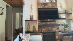 Una sala de estar con chimenea de piedra, televisor montado y un comedor al fondo.