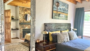 Un dormitorio con cabecera de madera, un espejo grande, un cuadro de un molino y vista a un muro de piedra.