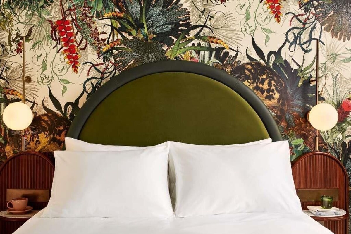A bed with white linens, a green upholstered headboard, and a floral wall mural.