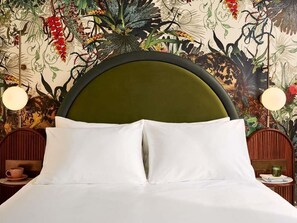 A bed with white linens, a green upholstered headboard, and a floral wall mural.