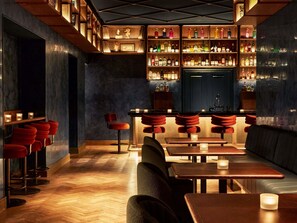Una zona de bar con estantes de madera, taburetes de bar rojos y mesas con velas.