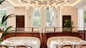 Restaurante com teto alto, luminárias pendentes e vista para uma igreja através de janelas em arco.