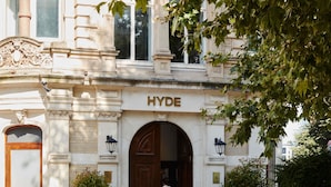 Um edifício com uma grande entrada em arco, um letreiro 'HYDE' acima da porta e dois vasos de plantas de cada lado da entrada.