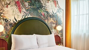 A neatly made bed with white linens and pillows, a green upholstered headboard, and a floral mural on the wall behind. - Hyde London City - St Paul’s (London)