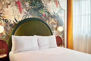 A neatly made bed with white linens and pillows, a green upholstered headboard, and a floral mural on the wall behind. - Hyde London City - St Paul’s (London)