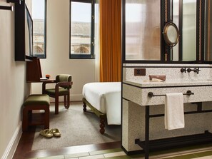 A hotel room with a bed, a desk, a chair, a bathroom with a sink and mirror, and a view of a building outside. - Hyde London City - St Paul’s (London)