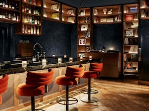 A bar area with wooden shelves, bar stools, and a counter. - Hyde London City - St Paul’s (London)