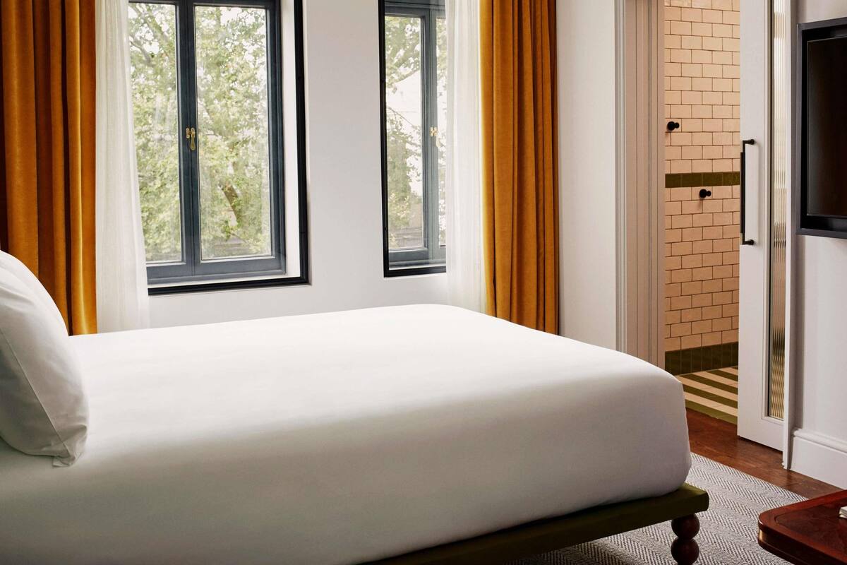 Une chambre d’hôtel avec un lit, deux fenêtres, une porte et un téléviseur.