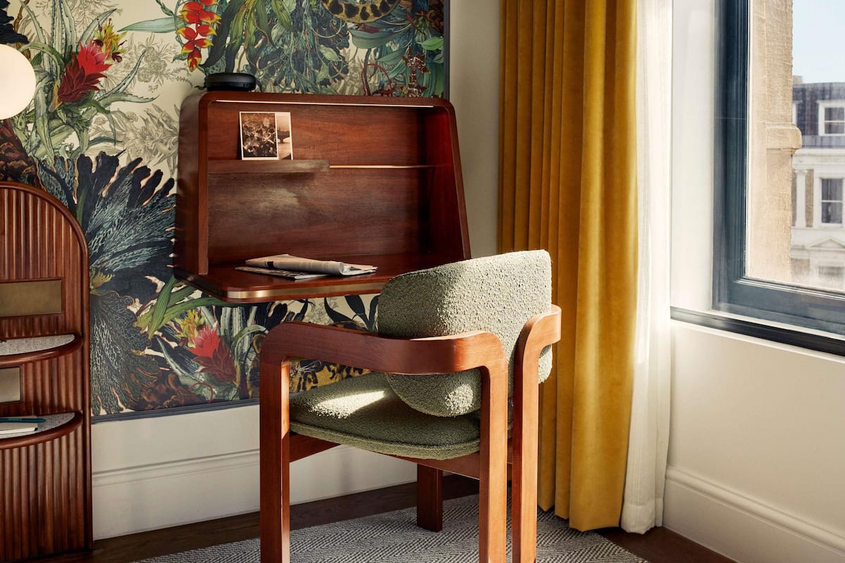 Une pièce d’angle avec une chaise en bois, un bureau et une fenêtre avec des rideaux.
