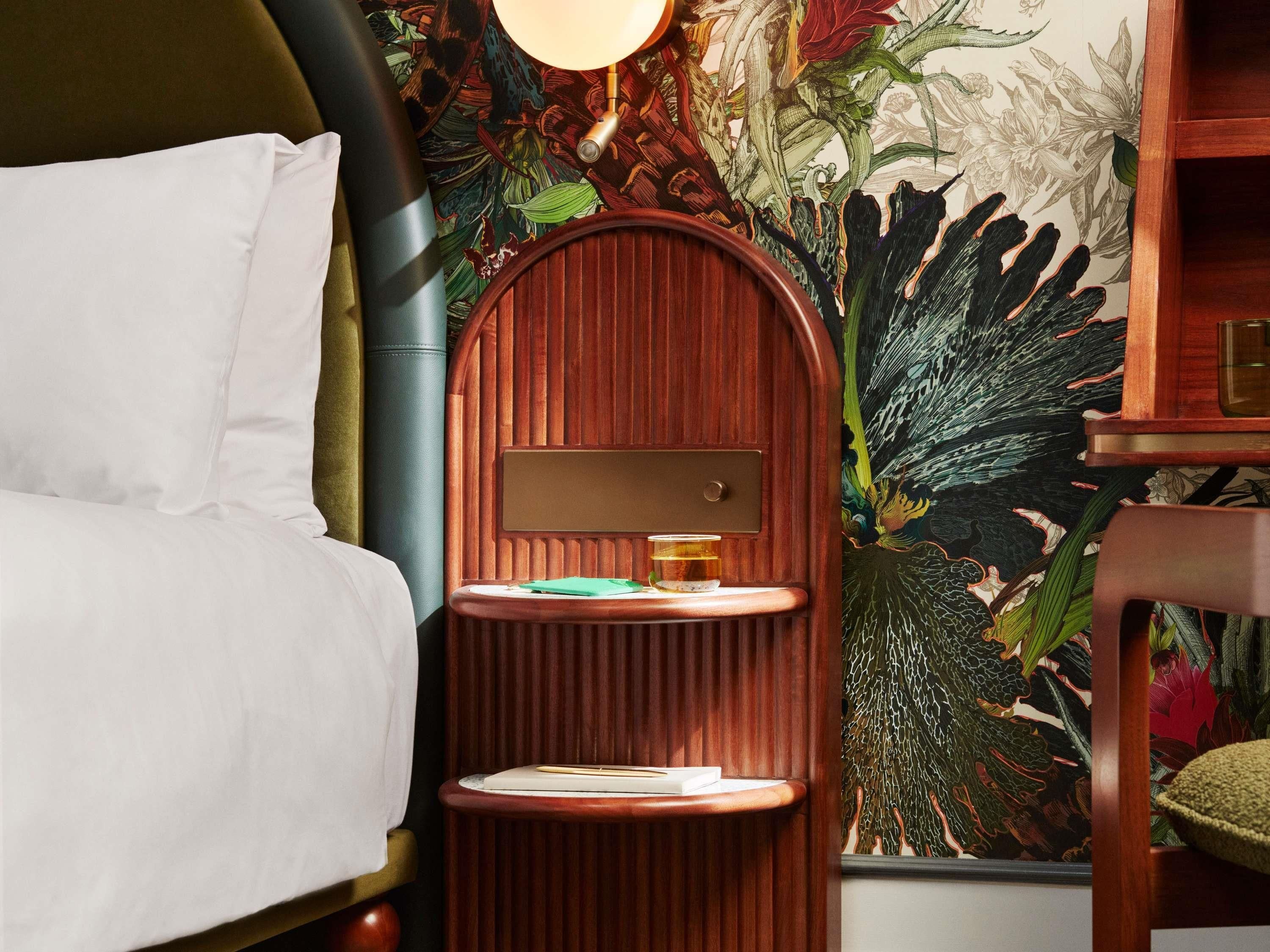 A bed with white linens, a wooden nightstand with a lamp, and a wall with a floral wallpaper.