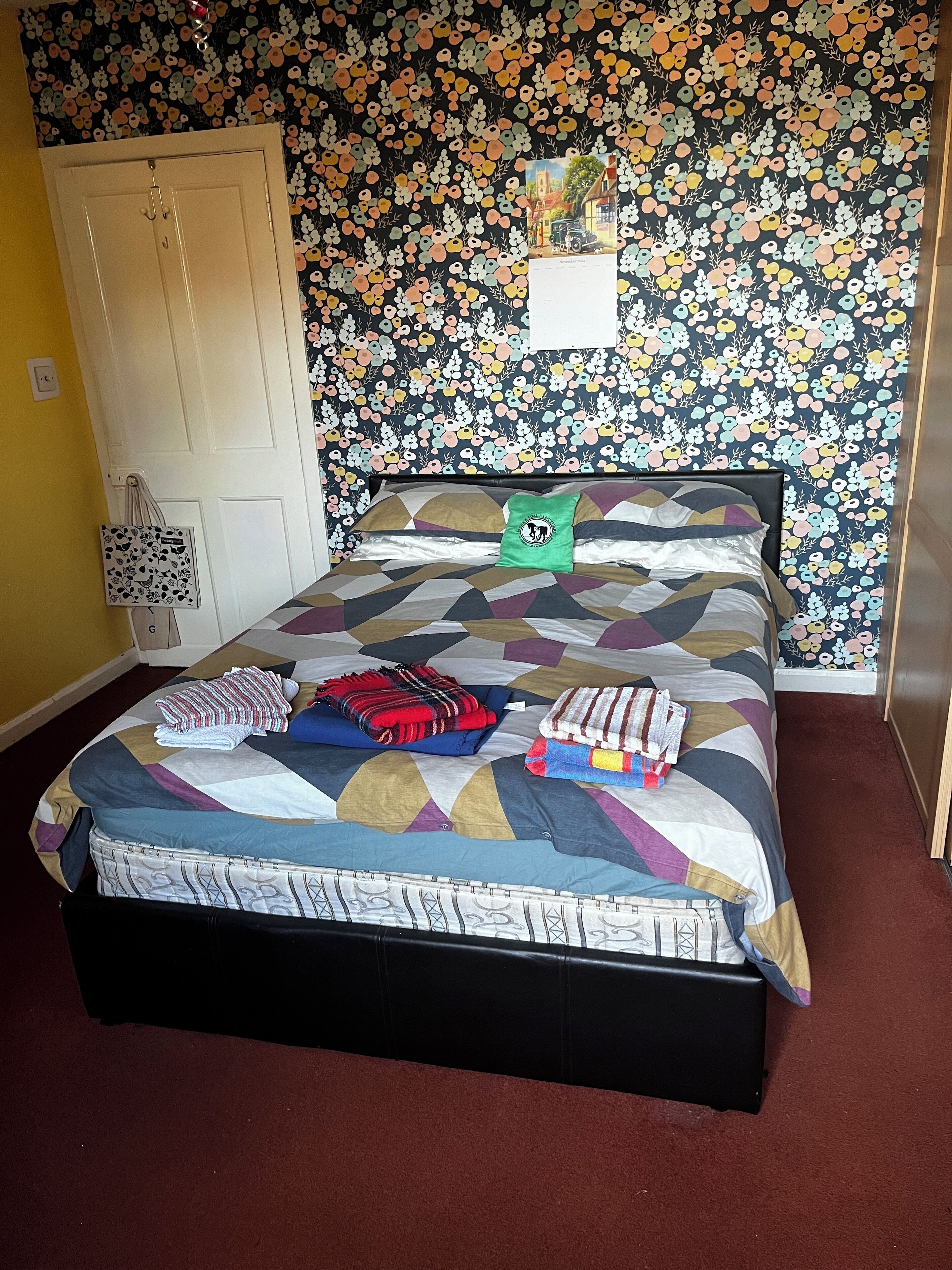 A bed with a patterned quilt, pillows, and folded blankets. A small green pillow is on the bed.