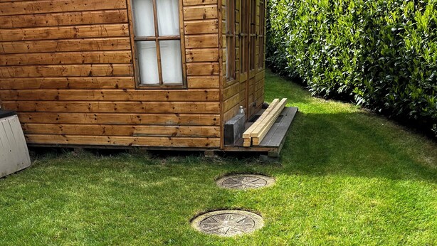 A wooden cabin with a grassy yard and four circular stepping stones leading to a door.