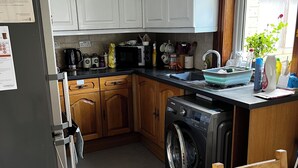 A compact kitchen with white cabinets, a built-in washing machine, and a dining area with a wooden table.