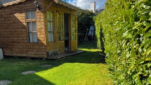 A wooden cabin with a porch, a small yard, and a hedge.