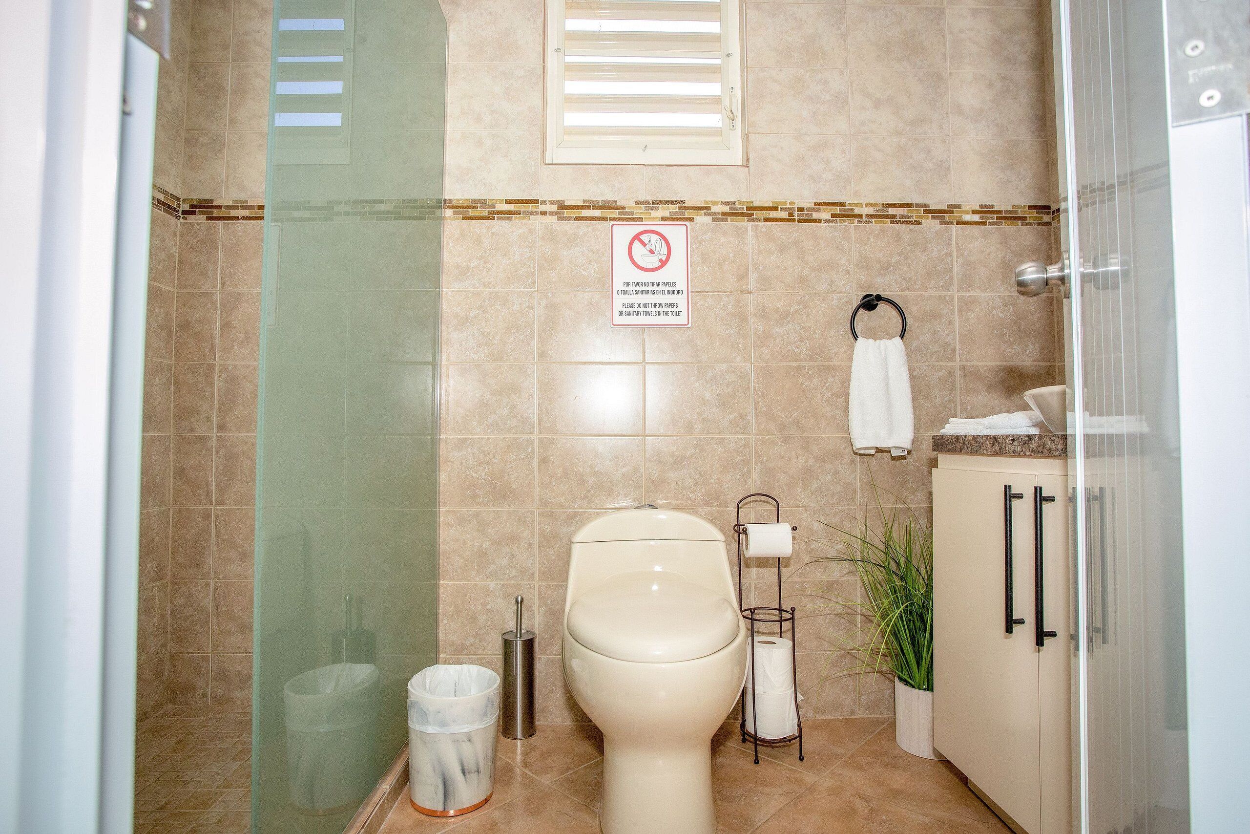 A bathroom with a toilet, a trash can, a towel rack, and a shower area.