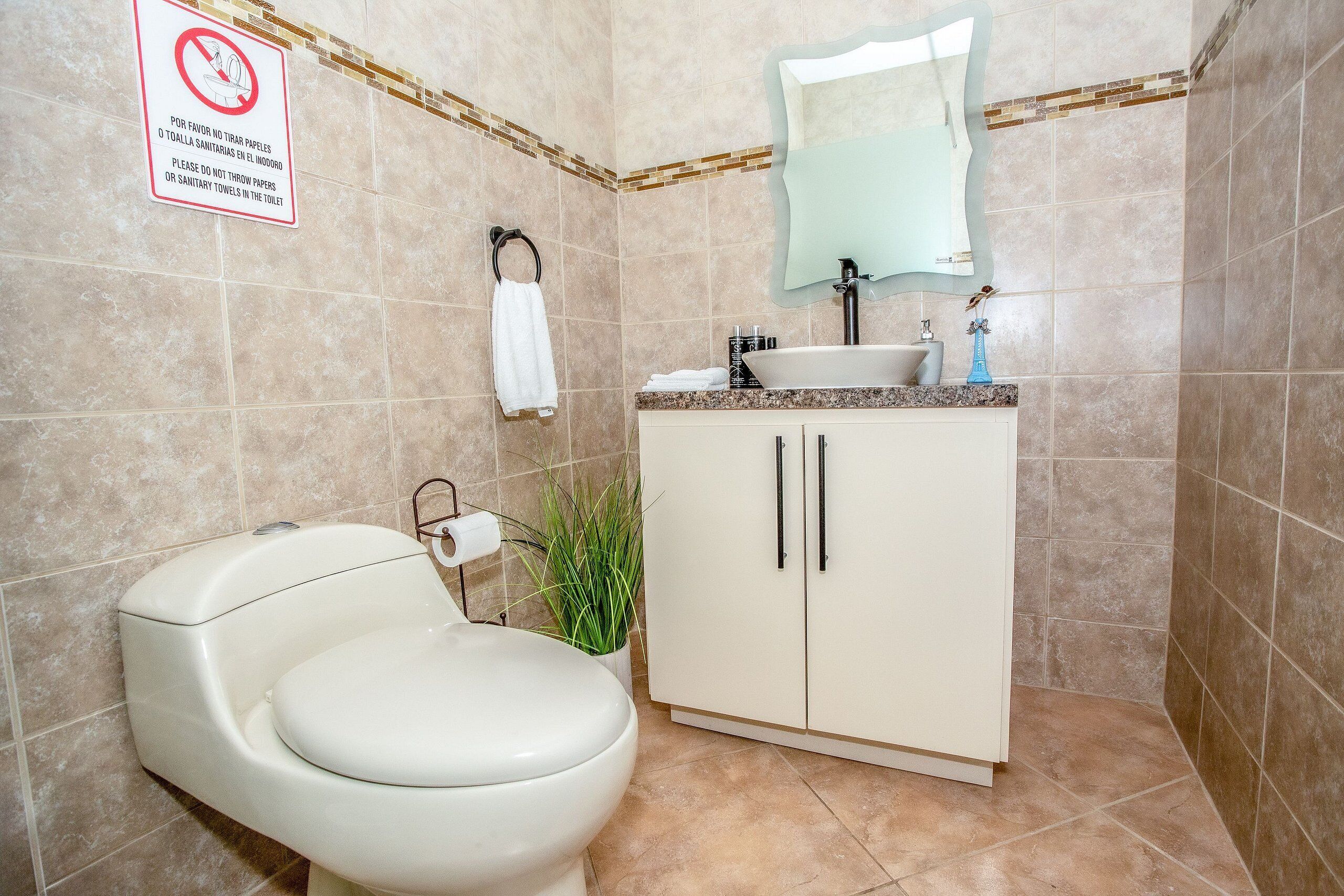 Ein Badezimmer mit Toilette, Waschbecken, Schrank und einem Schild, das die Entsorgung von Damenbinden in der Toilette untersagt.