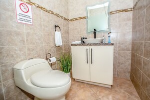 Baño con inodoro, lavamanos, armario y un cartel que prohíbe tirar toallas sanitarias en el inodoro.