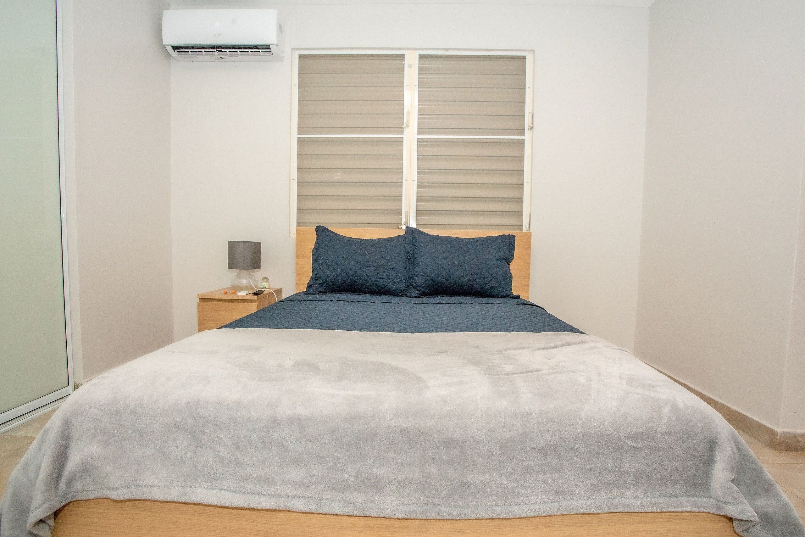 A bedroom with a bed, a nightstand, a lamp, and a window with blinds.