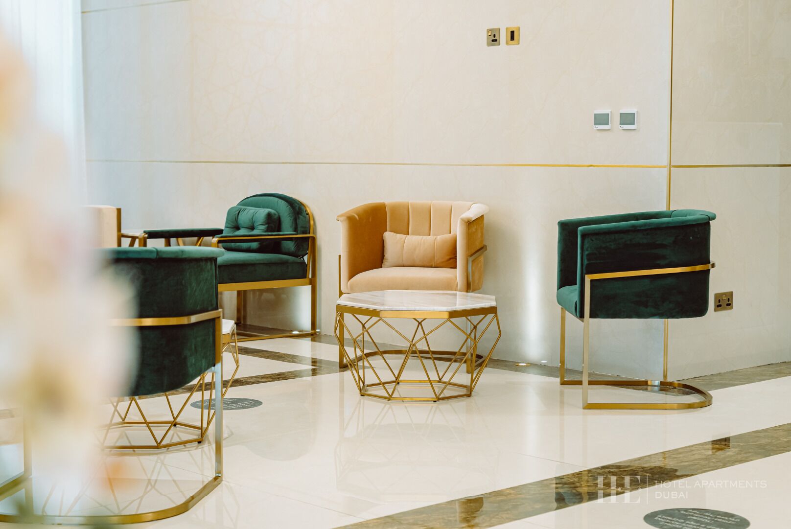 A modern hotel lobby with a beige sofa, green armchairs, and a gold-framed coffee table.