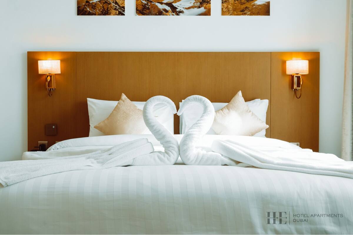 A hotel room with a neatly made bed, two wall-mounted lamps, and a wooden headboard.