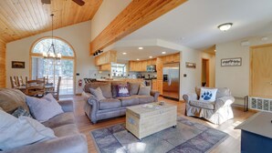A spacious living area with a high ceiling, wooden beams, a large arched window, and a view of the kitchen. - 4 Mi to Downhill Ski Resort! Spacious Family Haven (Truckee)