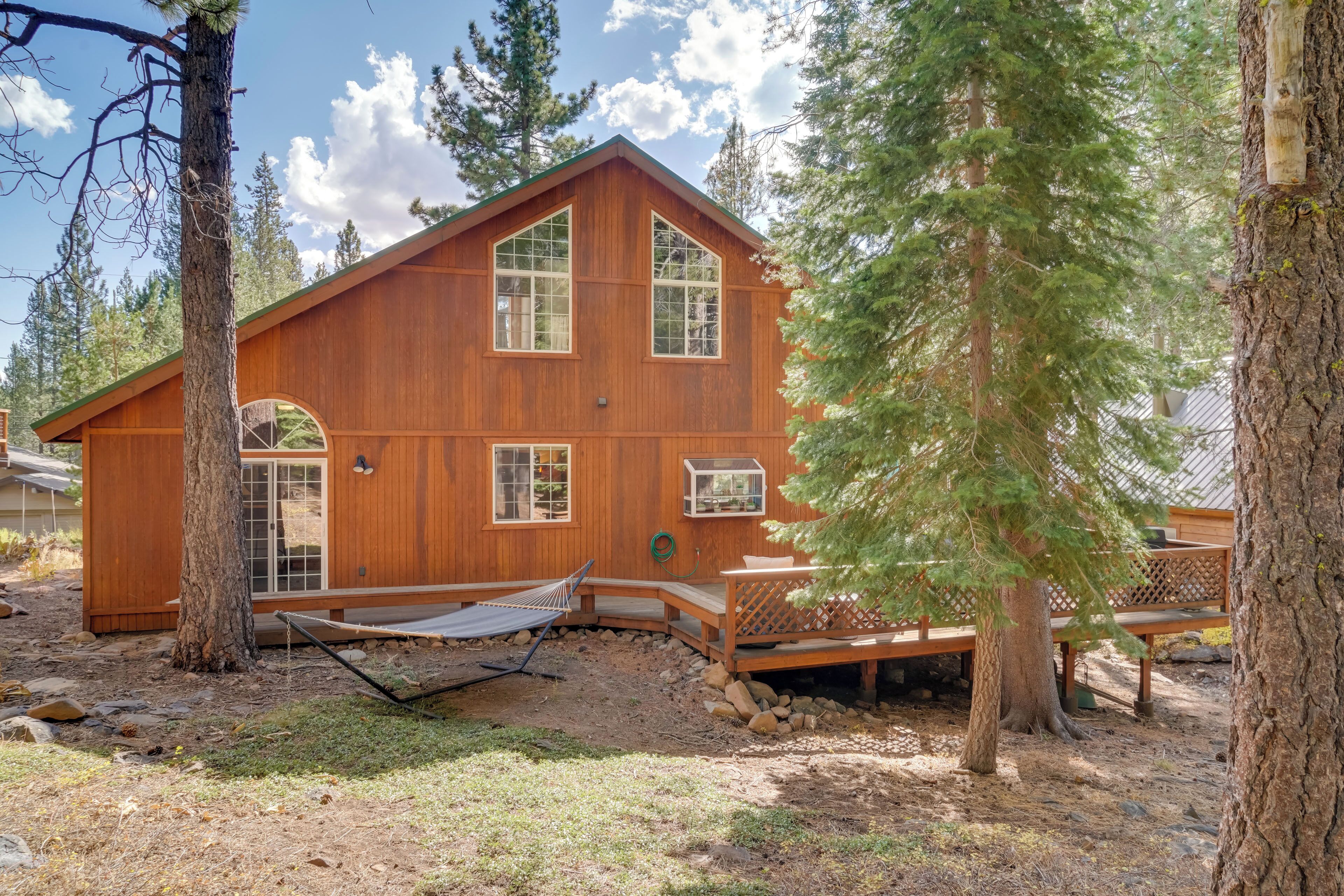 A wooden cabin with a large deck, surrounded by trees.