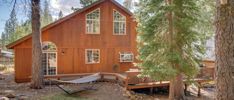 A wooden cabin with a large deck, surrounded by trees.