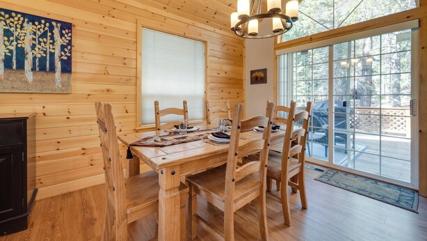 A wooden dining table with chairs, a chandelier, and a large window with a view of trees. - 4 Mi to Downhill Ski Resort! Spacious Family Haven (Truckee)