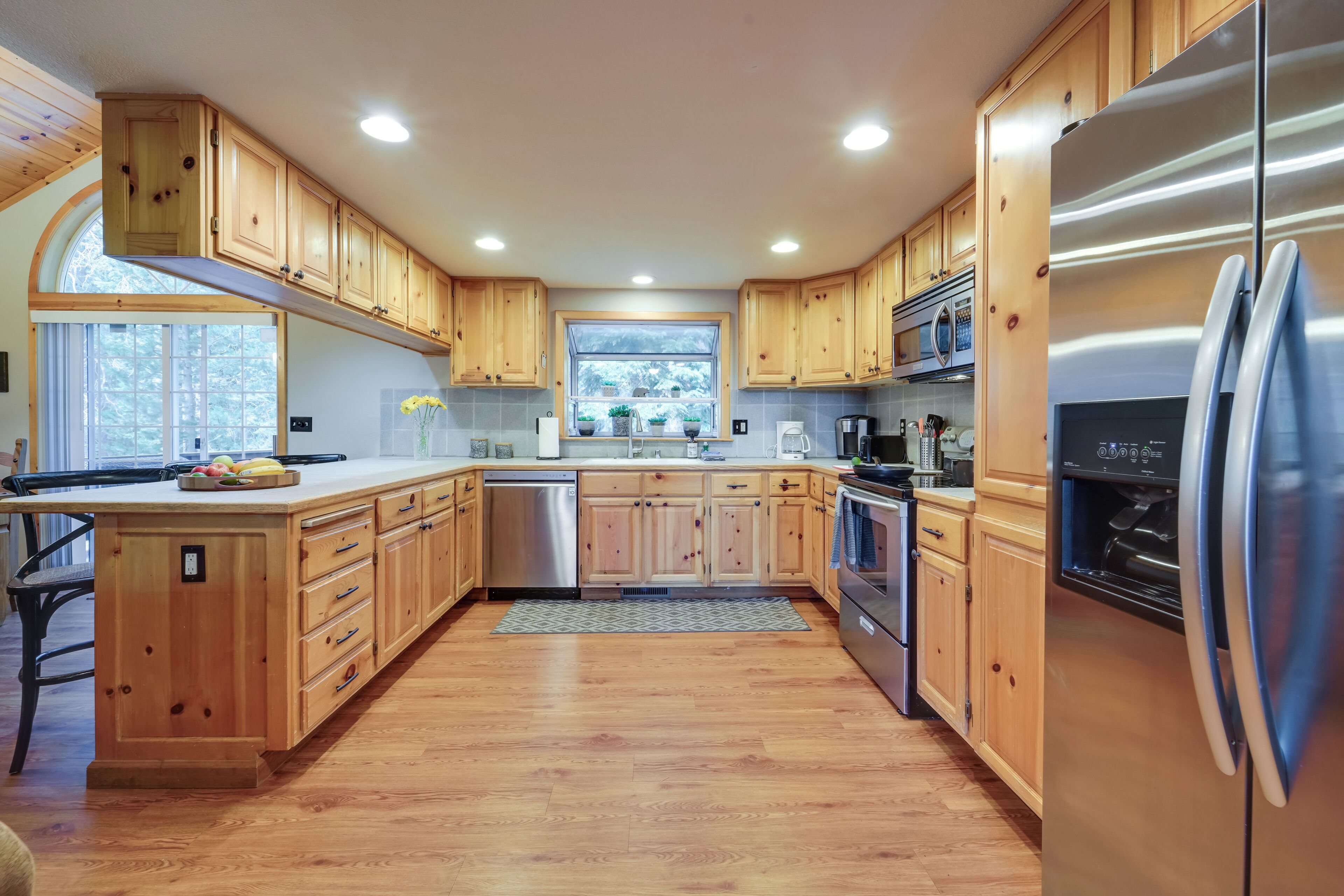 A modern kitchen with wooden cabinets, stainless steel appliances, and a large window providing natural light.