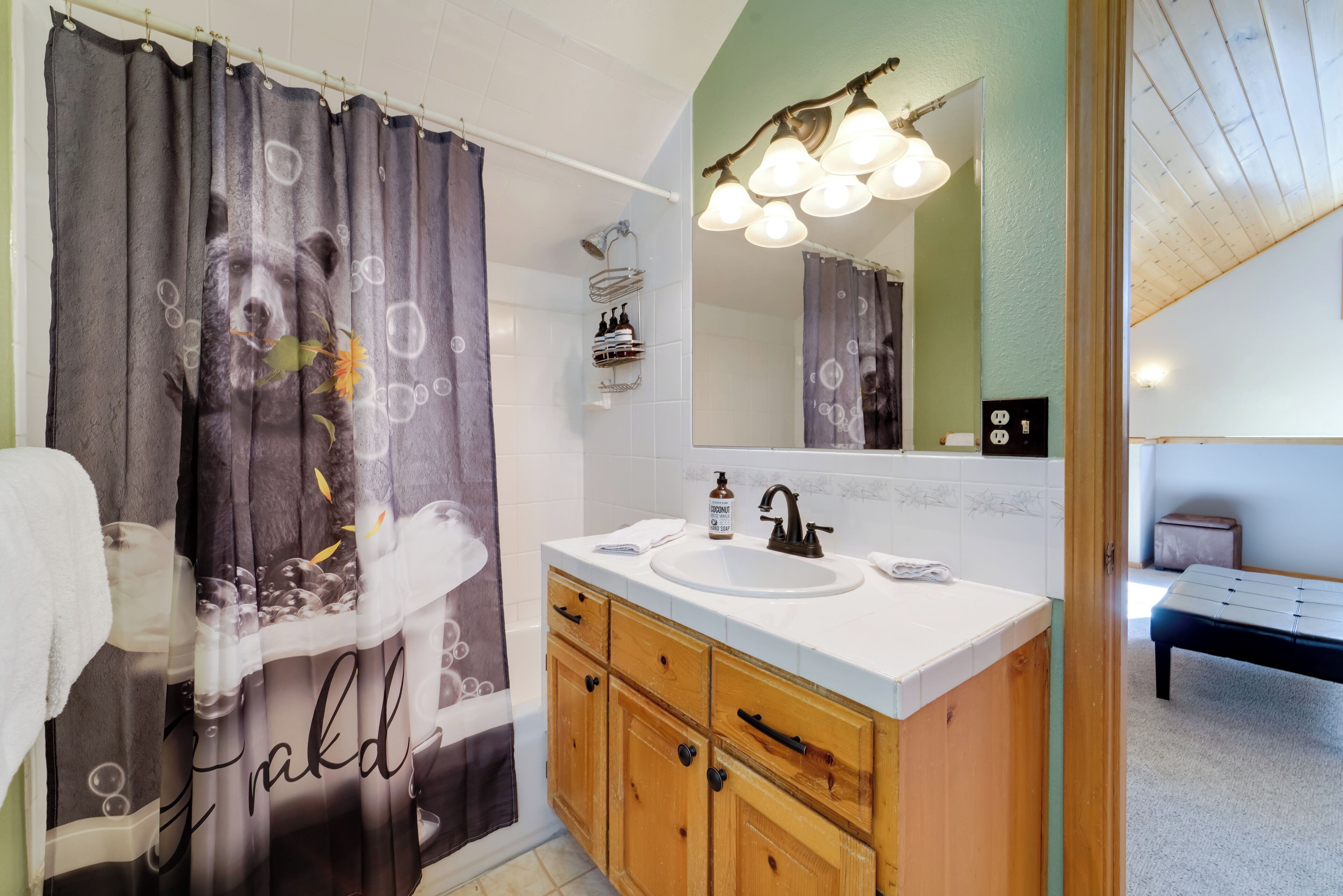 A bathroom with a wooden vanity, a white sink, a mirror above the sink, and a shower curtain with a bear design.