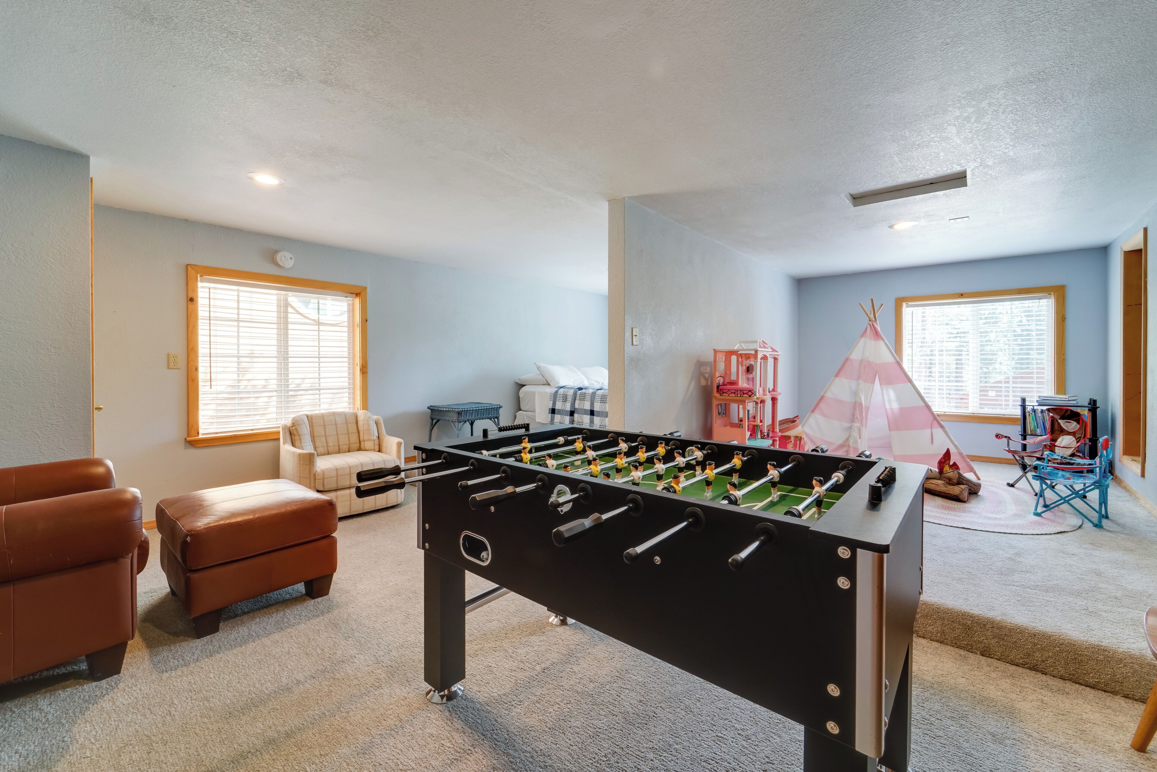 A room with a foosball table, a brown leather sofa, a small ottoman, and a teepee tent.