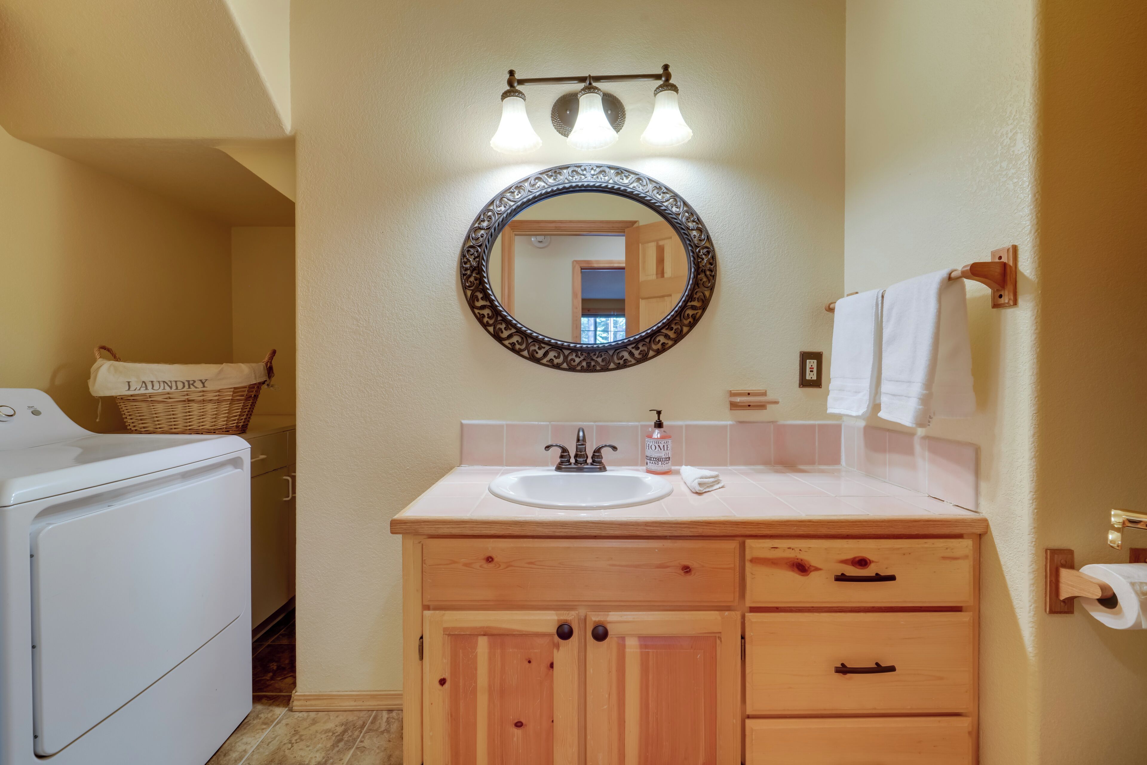 A bathroom with a sink, mirror, and wooden cabinets. There is a laundry basket and a washing machine in the background.