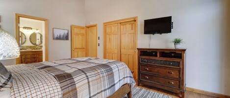 Un dormitorio con cama, armario de madera, televisor de pantalla plana y ventilador de techo.