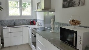 Een moderne keuken met witte kastjes, een zwarte magnetron en een raam met uitzicht op groen.