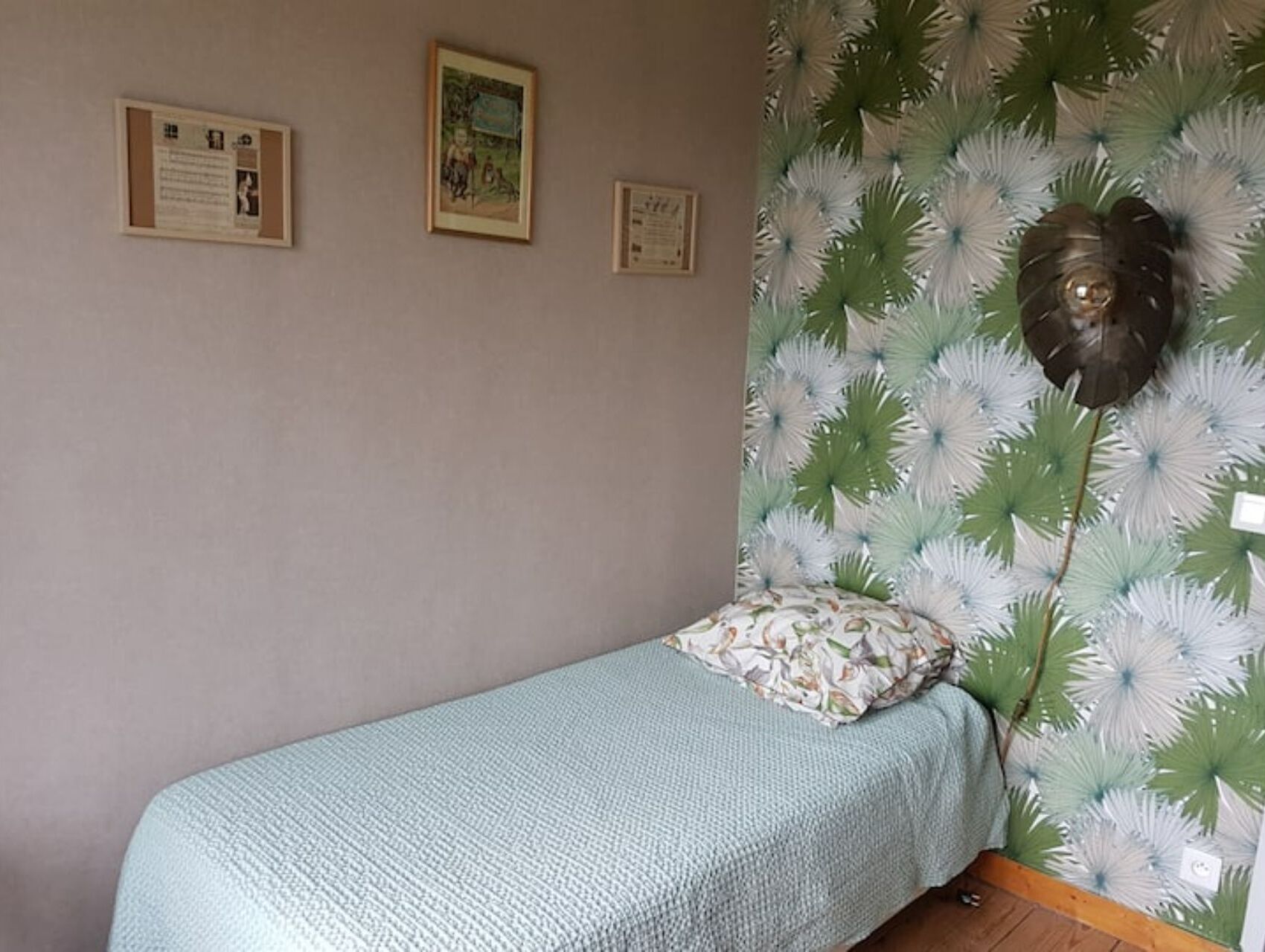 A small bedroom with a single bed, a wall with framed certificates, and a decorative wall hanging.